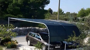 En sort SUV parkeret i en indkørsel med en stenvæg og en metalkonstruktion over sig.