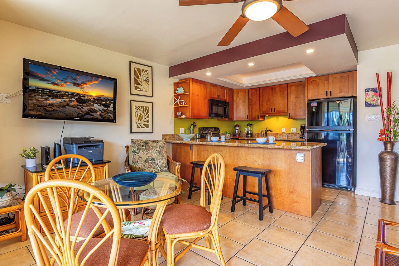 Una cocina moderna con armarios de madera, una isla central y un comedor con sillas de mimbre.