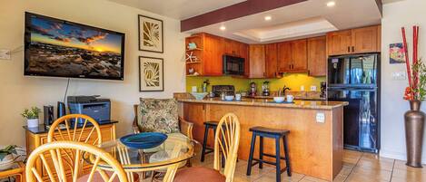 Una cocina moderna con armarios de madera, una isla central y un comedor con sillas de mimbre.
