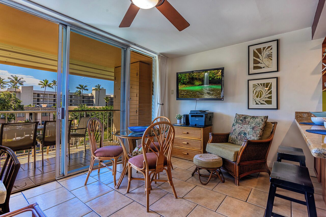 Een balkon met een eethoek, rieten stoelen, een televisie en kunst aan de muur.