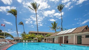 Una piscina con sillas de descanso y palmeras, rodeada de edificios con techo de tejas.