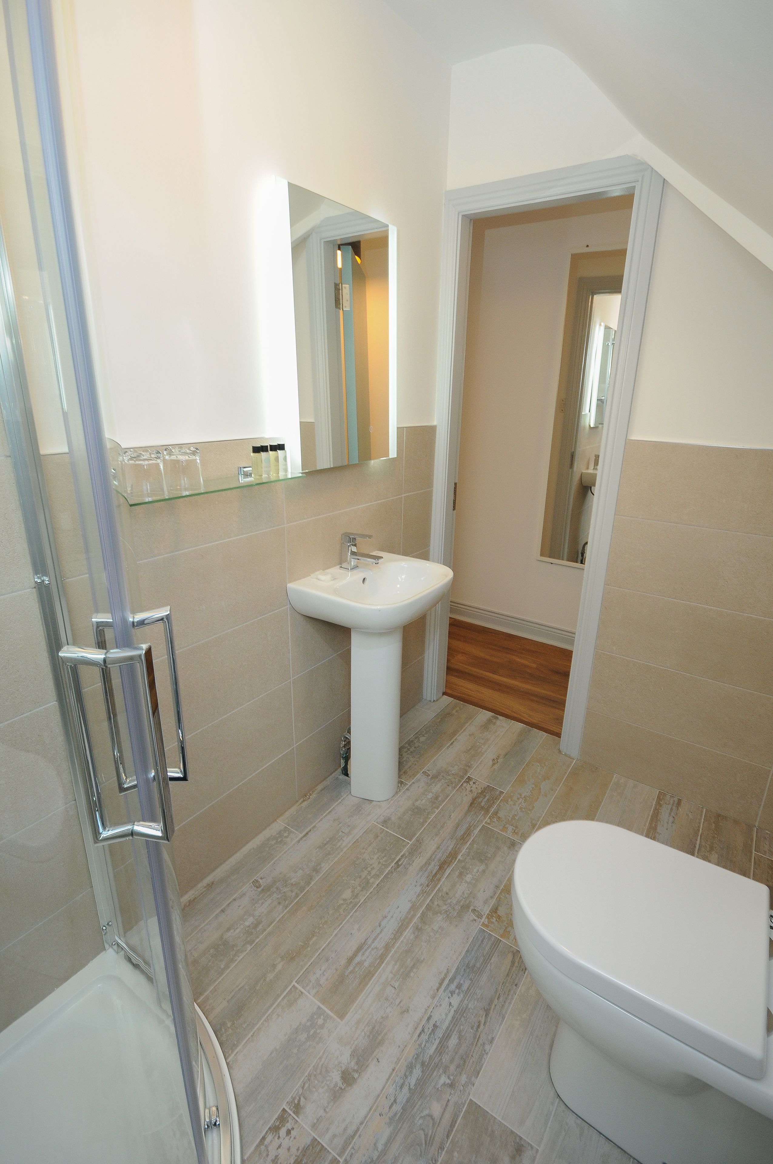Een badkamer met een douchecabine van glas, een wastafel op voet en een toilet.