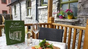 A table set with a plate of food, a wine glass, and a menu at a restaurant with stone walls and wooden furniture. - Lodge at The Old Barracks (Athenry)