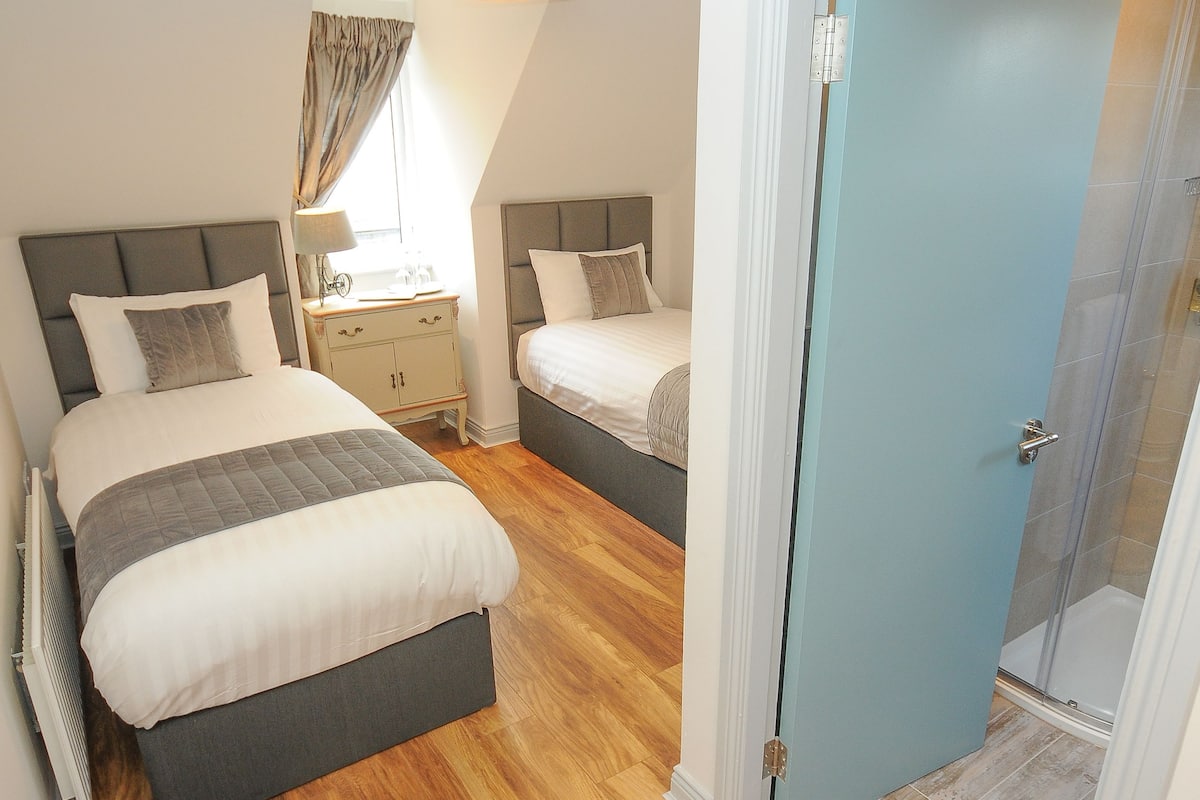 A bedroom with two beds, a nightstand, a lamp, and a door leading to a bathroom.