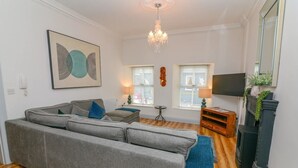A living room with a sectional sofa, a chandelier, a television, and a fireplace. - Lodge at The Old Barracks (Athenry)