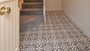 A staircase with carpeted steps, a chandelier, and patterned floor tiles. - Lodge at The Old Barracks (Athenry)