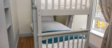Ein Stockbett mit Fenster und Vorhängen, Holzboden und einem Regal.