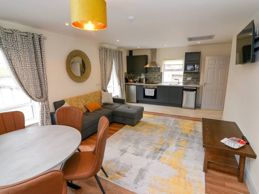 A modern living room with a grey sofa, a dining table with chairs, and a kitchen in the background.