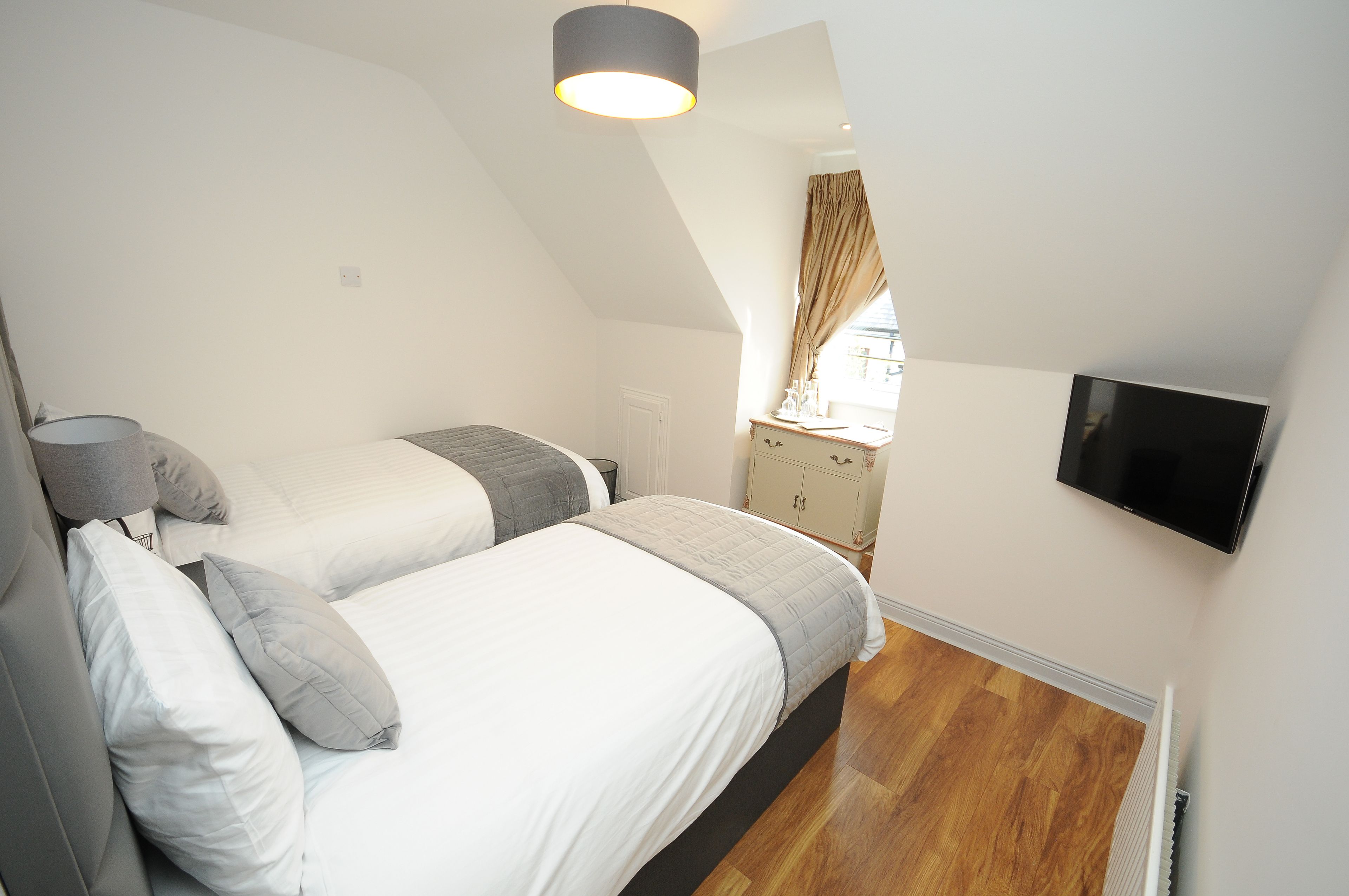 A bedroom with two beds, a flat-screen TV, a window with curtains, and a radiator.