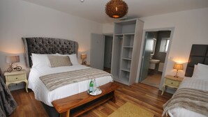 A bedroom with a large bed, bedside tables, a wardrobe, and a bathroom visible through an open door. - Lodge at The Old Barracks (Athenry)