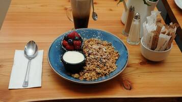 A breakfast setting with a plate of granola, berries, and yogurt, a cup of coffee, and condiments on a wooden table.