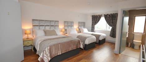 A bedroom with two beds, wooden flooring, and a bathroom with a toilet and sink.