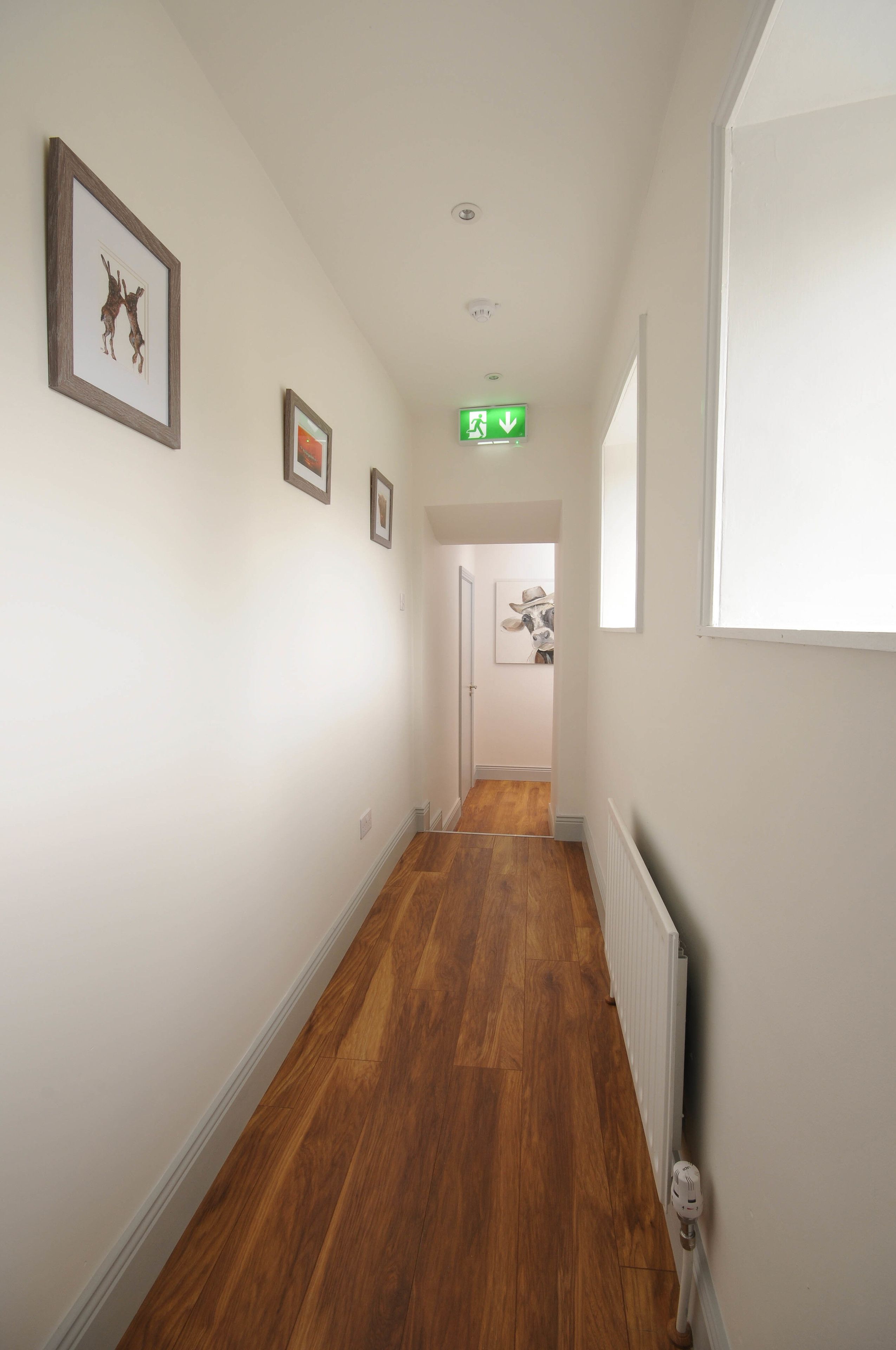Un couloir doté d’un plancher en bois, de murs blancs et de tableaux encadrés.
