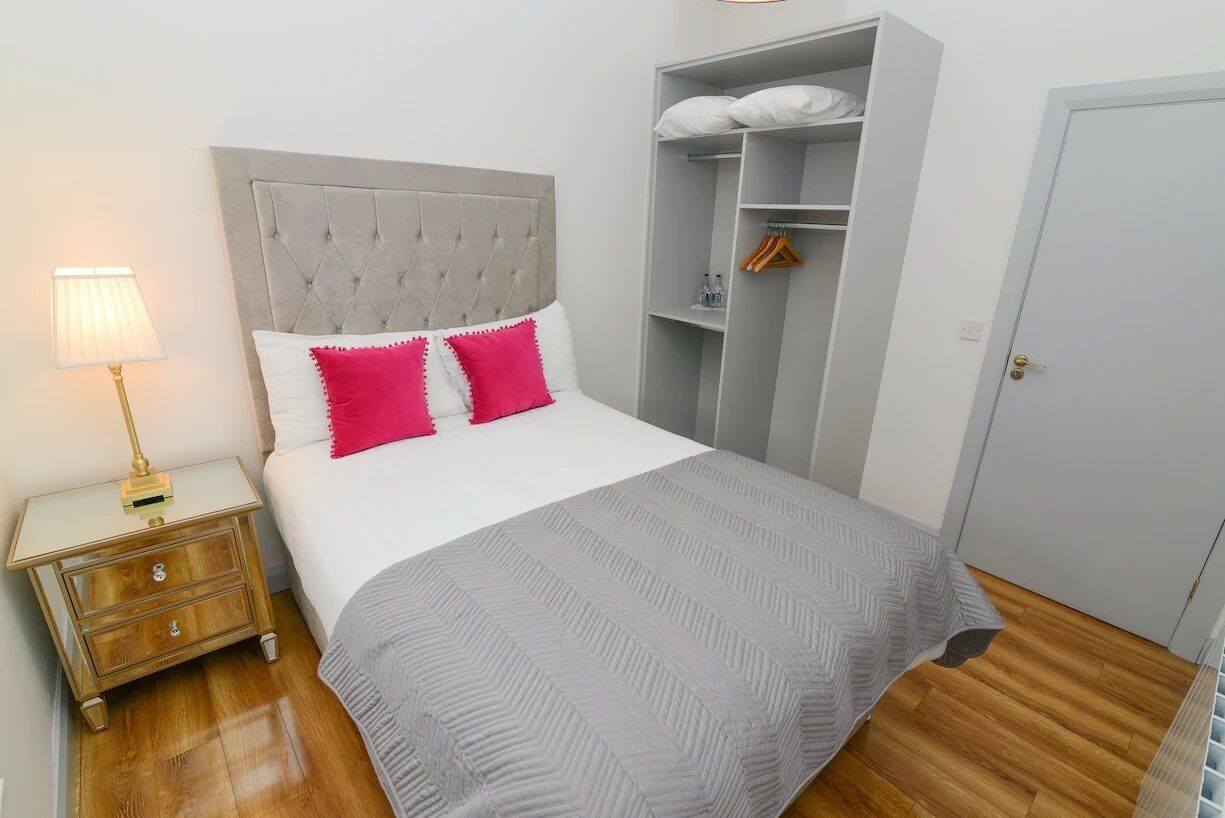 A neatly arranged bedroom with a bed, bedside table, lamp, wardrobe, and a door.