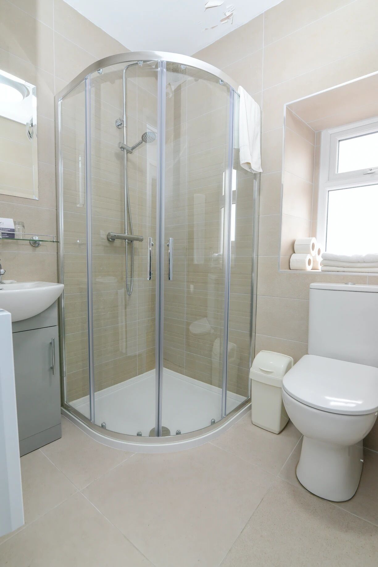A modern bathroom with a glass-enclosed shower, a white sink, a toilet, and a small window.
