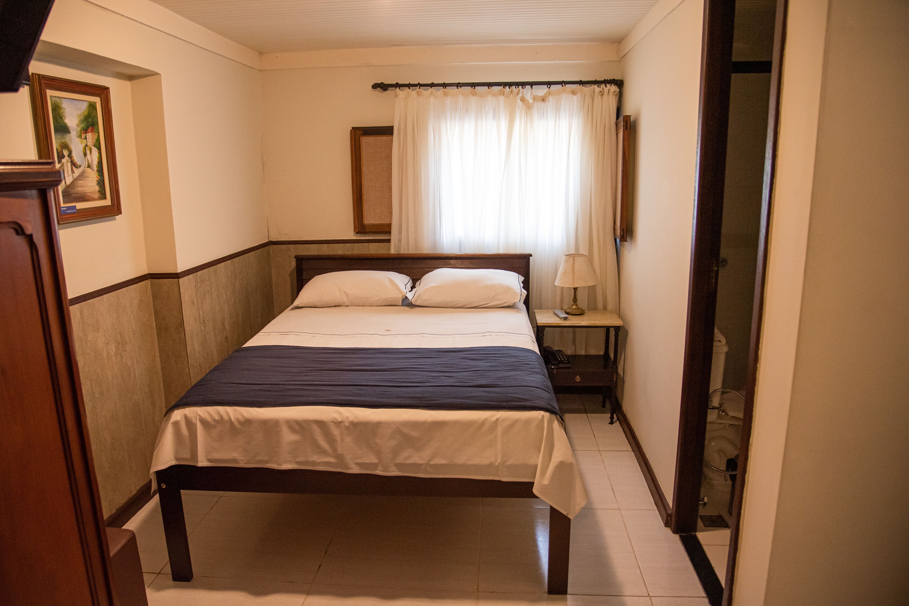 Um quarto com uma cama, mesa de cabeceira, abajur e porta para um banheiro.