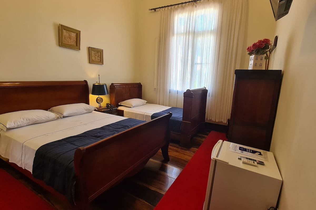 A hotel room with two single beds, a wooden wardrobe, a desk, and a small refrigerator.