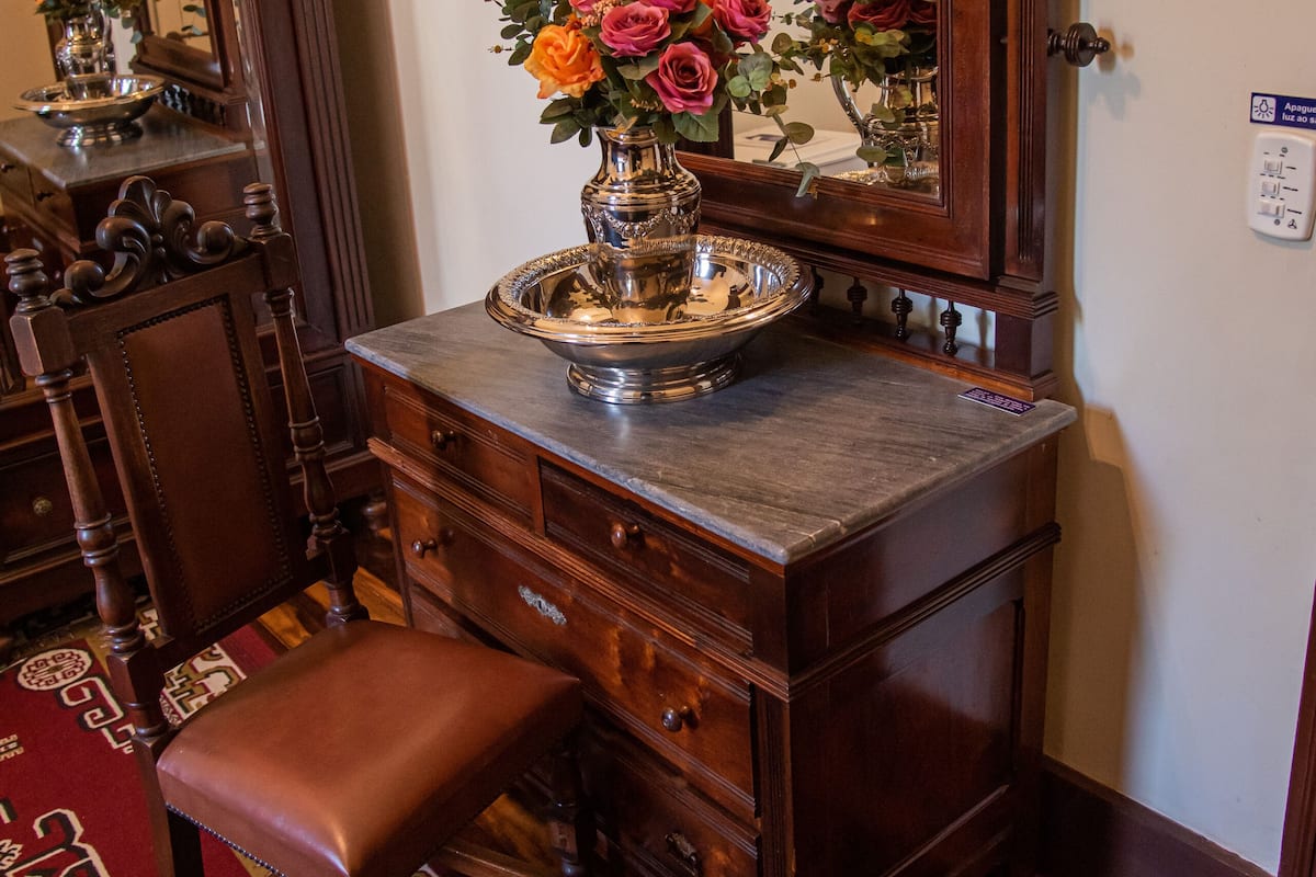 A wooden dresser with a mirror, a vase of flowers, and a tray.