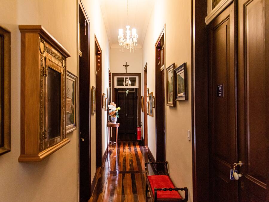 A hallway with wooden floors, framed pictures, and a chandelier.