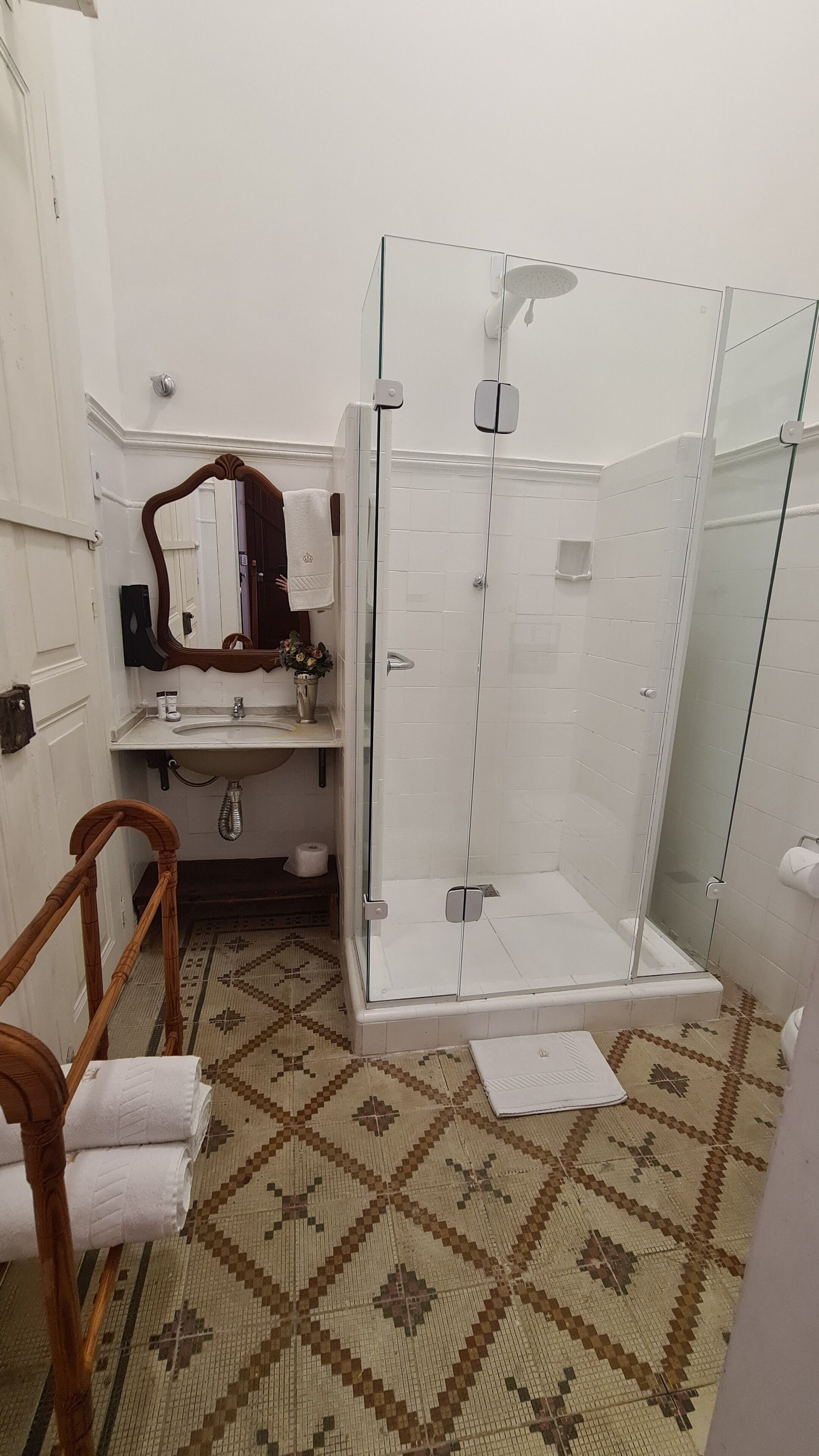 Un baño con cabina de ducha de vidrio, un lavabo con espejo y piso estampado.