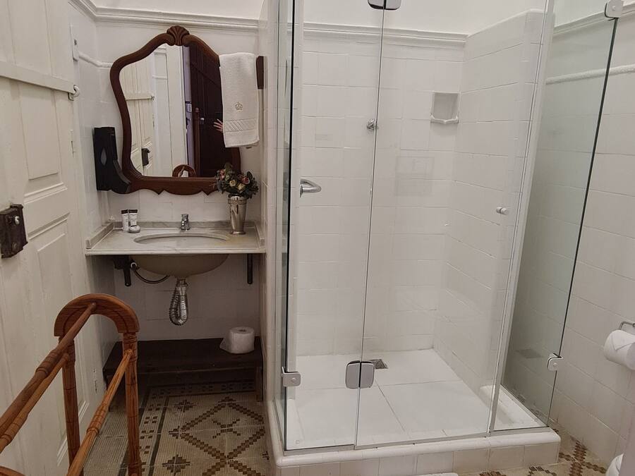 Un baño con cabina de ducha de vidrio, un lavabo con espejo y piso estampado.