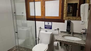 Een badkamer met een douchecabine van glas, een toilet, een wastafel met een granieten blad en een spiegel met een gouden lijst.