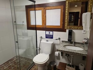 A bathroom with a glass shower enclosure, a toilet, a sink with a granite countertop, and a mirror with a gold frame. - Pousada Dom Petrópolis (Petrópolis)