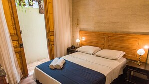 A hotel room with a wooden headboard, a bed with white and blue bedding, two bedside lamps, and a door leading to a balcony. - Pousada Dom Petrópolis (Petrópolis)
