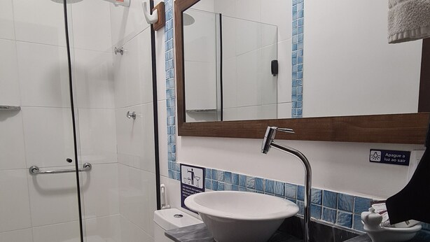 A bathroom with a white toilet, a sink with a marble countertop, a wooden vanity, a mirror, and a shower area. - Pousada Dom Petrópolis (Petrópolis)
