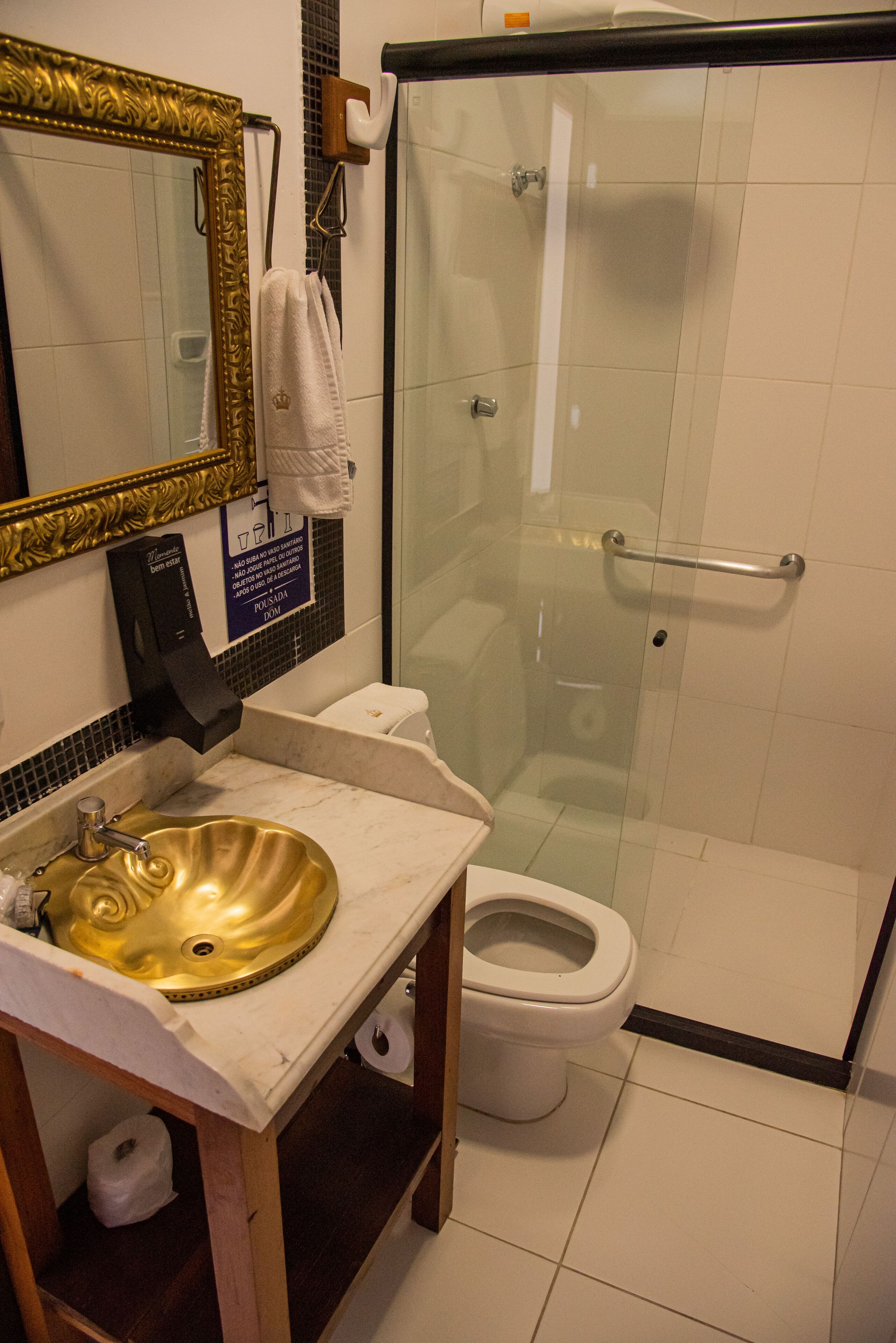 Un baño con lavamanos dorado, inodoro blanco y ducha con mampara de vidrio.