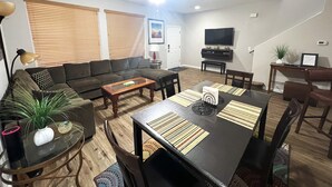 Un salon comprenant un canapé, une table basse, une table à manger, des chaises, un téléviseur et un ventilateur de plafond.