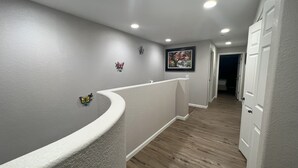 Un couloir doté d’une rambarde blanche incurvée, d’un plancher en bois et de spots encastrés au plafond.