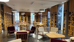 Una biblioteca con estanterías de madera, mesas y sillas, y una pantalla grande que muestra una imagen.