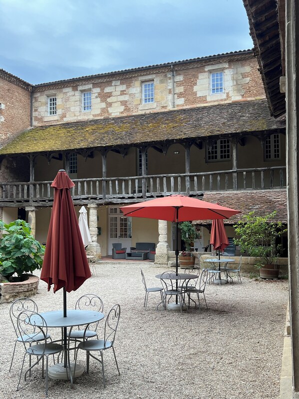 A courtyard with stone buildings, outdoor seating, and umbrellas.