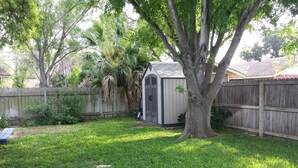 Ein Garten mit Holzzaun, Gartenhaus und Baum.