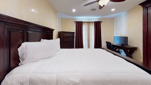 Ein Hotelzimmer mit einem großen Bett, einer Holzkommode, einem Schreibtisch mit Fernseher und einem Deckenventilator.