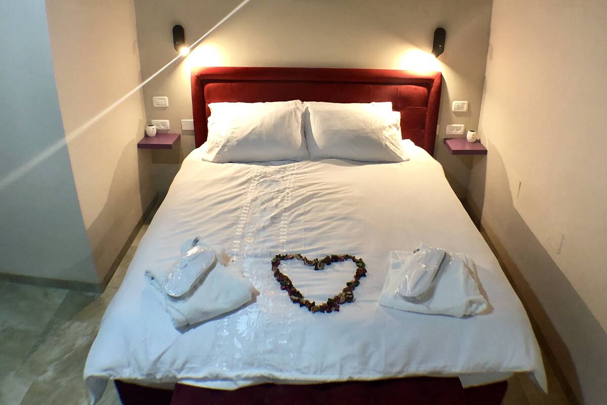 A neatly made bed with white linens and a heart-shaped arrangement of flowers on the bedspread.