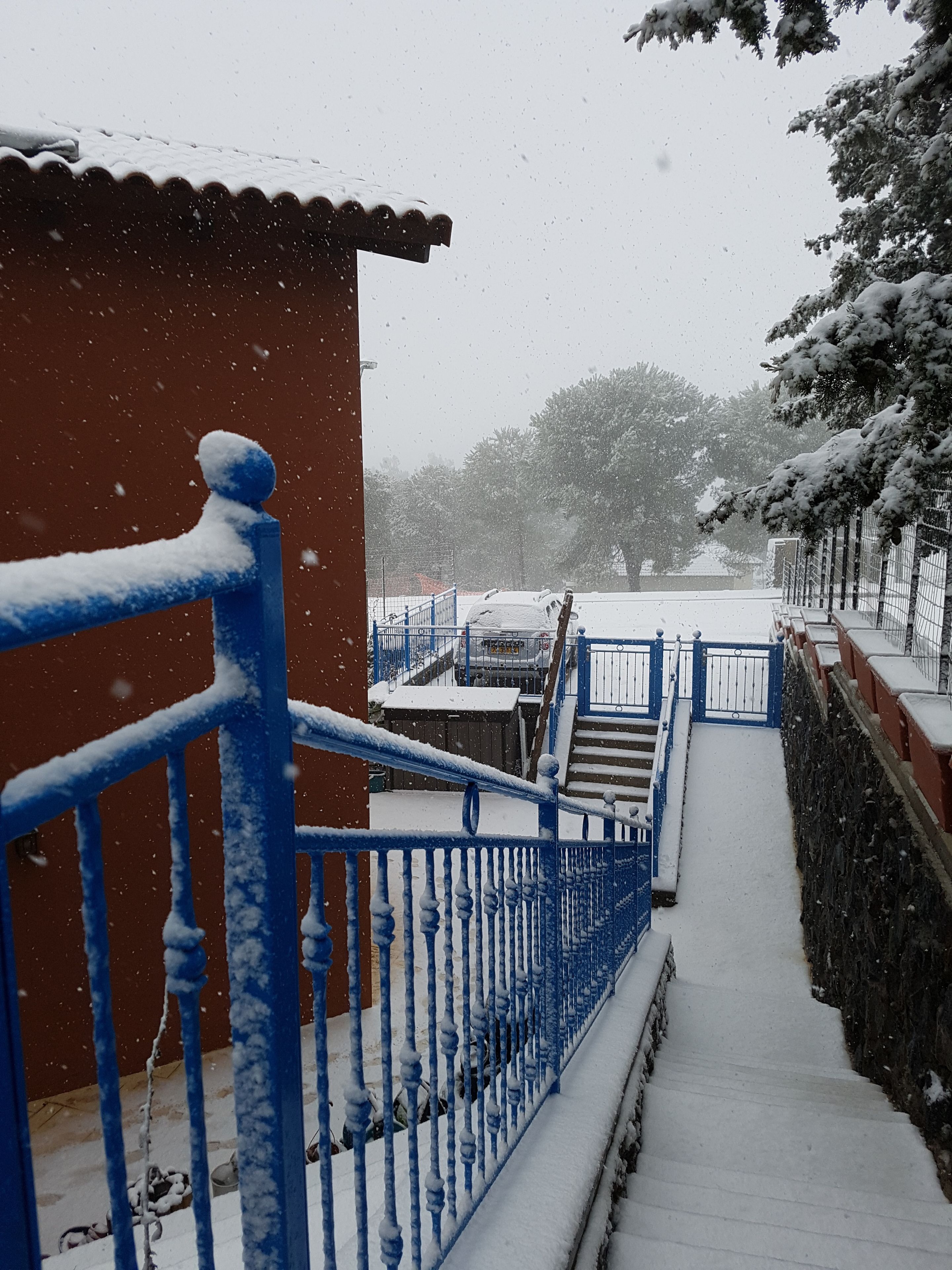 A snow-covered outdoor staircase leading to a building with a red wall and blue railings.