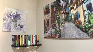 Una pared con un cuadro de una calle empedrada, una estantería con libros y una obra de arte con temática lavanda.