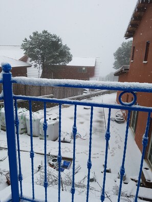 Escena nevada con una barandilla de metal azul, un edificio y un árbol al fondo.
