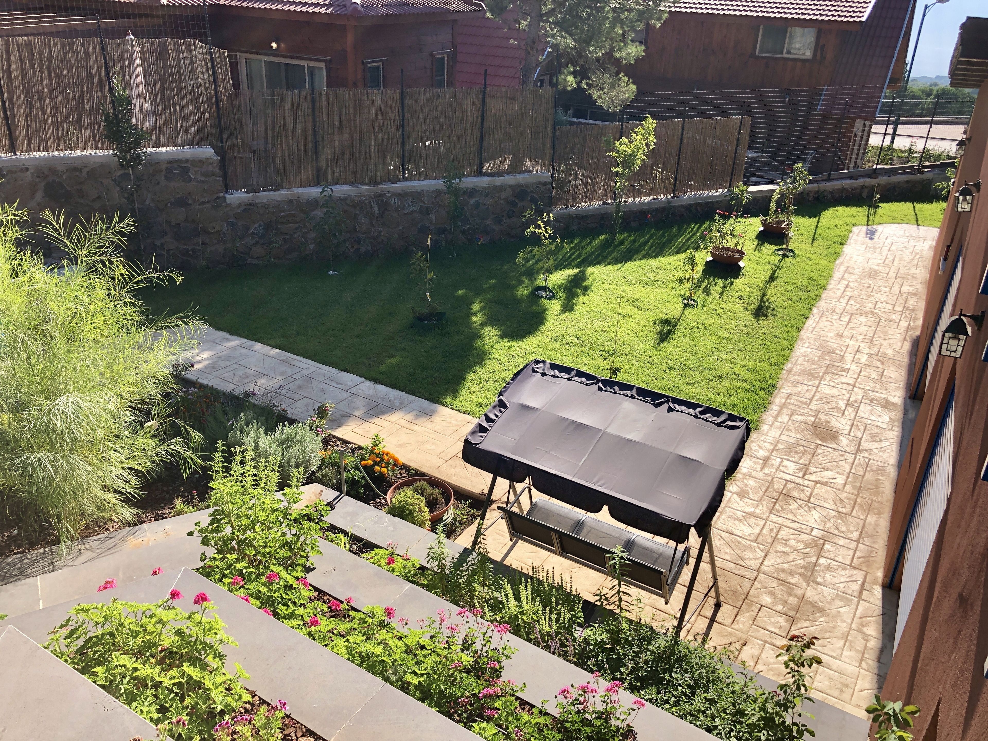 Un patio trasero con un camino de piedra, zona de barbacoa y un pequeño jardín con flores.