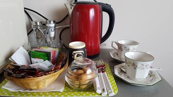 Una preparación para el desayuno con una tetera roja, tazas, una cesta de bocadillos y un tarro de cristal sobre un mantel de lunares verdes.