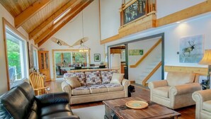 A spacious living room with a high ceiling, wooden beams, a fireplace, a dining area, and a staircase leading to an upper level.