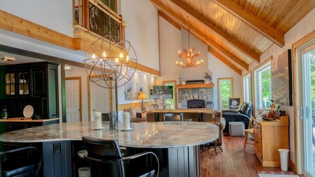 A spacious kitchen with a large island, wooden beams, and a stone fireplace.