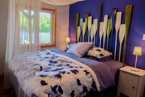 A bedroom with a bed, a nightstand, a window with a view of greenery, and a wall with decorative paddles.