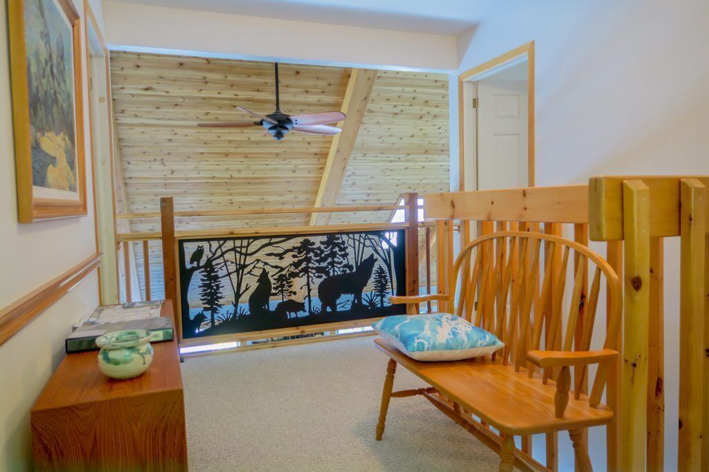Una habitación acogedora con techo inclinado, una silla de madera con cojín, una mesita con un cuenco y un cuadro en la pared de animales del bosque.