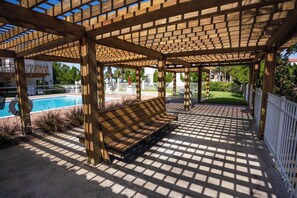 Relax in a serene poolside area surrounded by lush greenery and a shaded pergola.