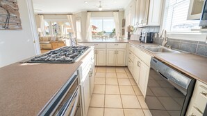 A kitchen with a stove, sink, and dishwasher, with a view to the outside. - Beach & Bay views! 4BR/3.5BA, Elevator, Com Pool/Tennis Court (St. George Island)
