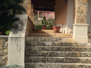 Steps lead to a traditional building with a Mediterranean-style facade and a window with a red frame.