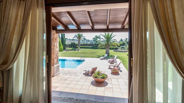 An open door to a pool area with a view of a well-maintained lawn and palm trees. - Luxurious villa Maremonti (Canicattini Bagni)